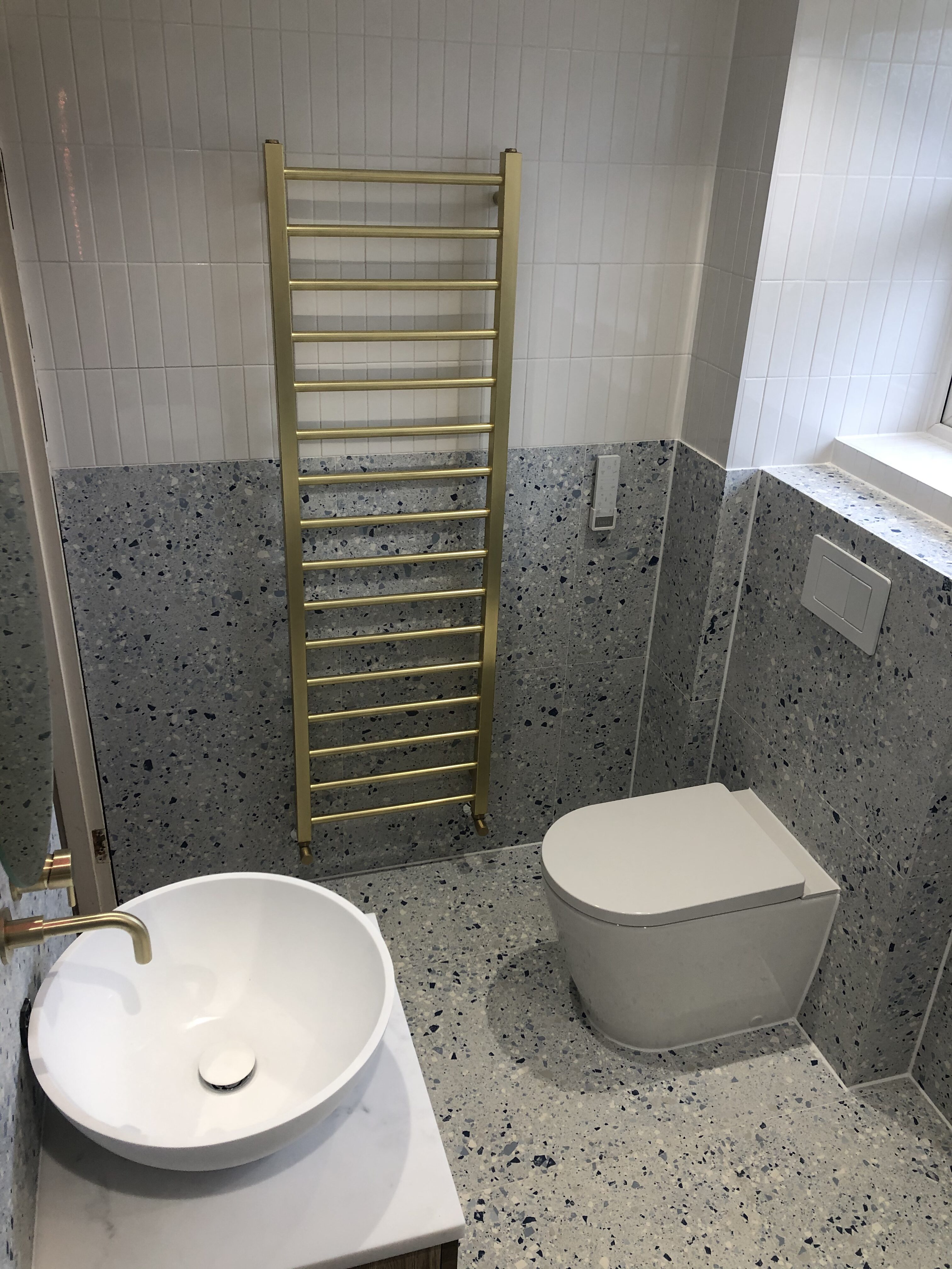 Cloakroom finished in grey terrazzo tiling with a brass heated towel rail and countertop basin