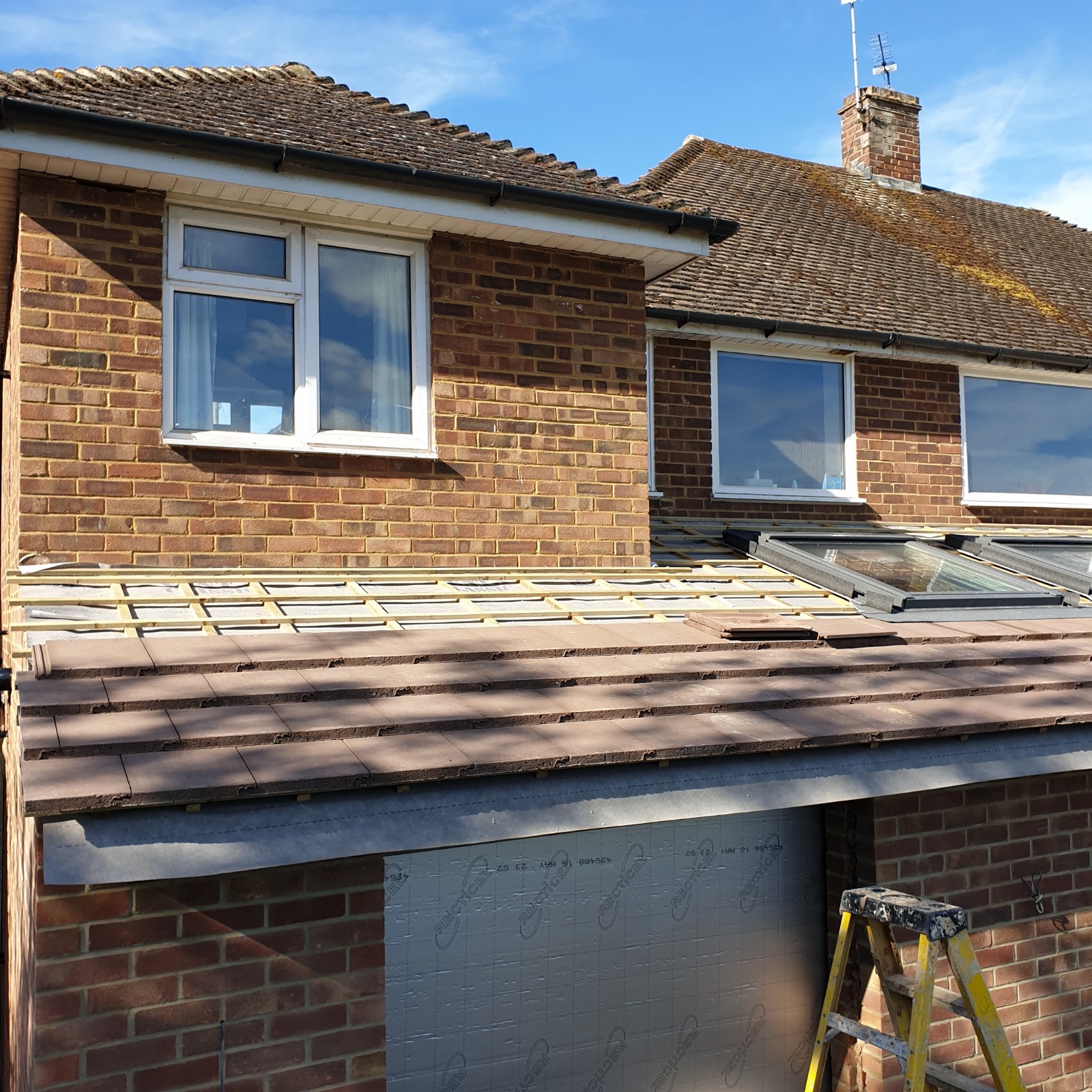 Extension roof under construction, with tiles part-laid over battens and a rooflight fitted