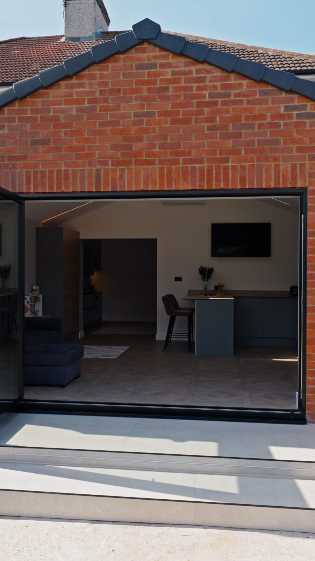 Rear extension with black bi-fold doors open onto a patio, looking through to the kitchen