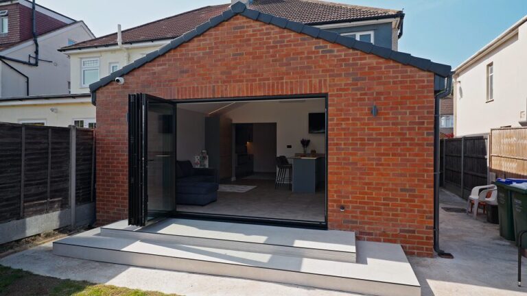 Brick rear extension with black bi-fold doors folded open onto a paved garden terrace