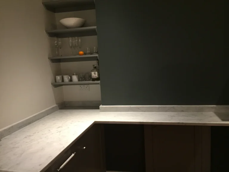 Corner of a dark kitchen with marble worktop and open shelving