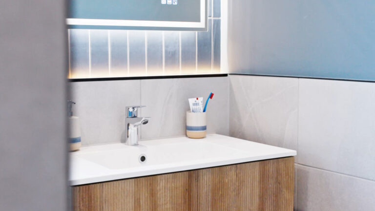 Vanity unit with a fluted wood cabinet, white basin and backlit mirror