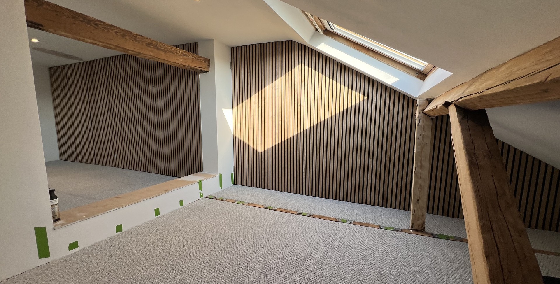 Finished loft room with exposed timber beams, slatted oak panelling, carpet and a rooflight, converted by Space Up