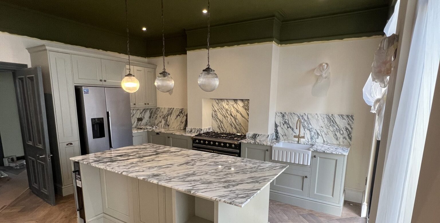 Finished kitchen in a Victorian house in South Norwood, marble island, pale shaker units and a herringbone floor under a dark green ceiling