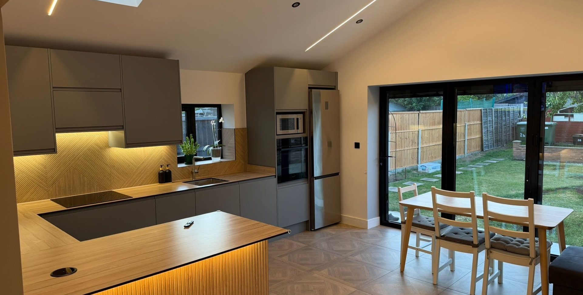 Finished kitchen extension near Dartford, black bifold doors onto the garden, island and warm under-cabinet lighting